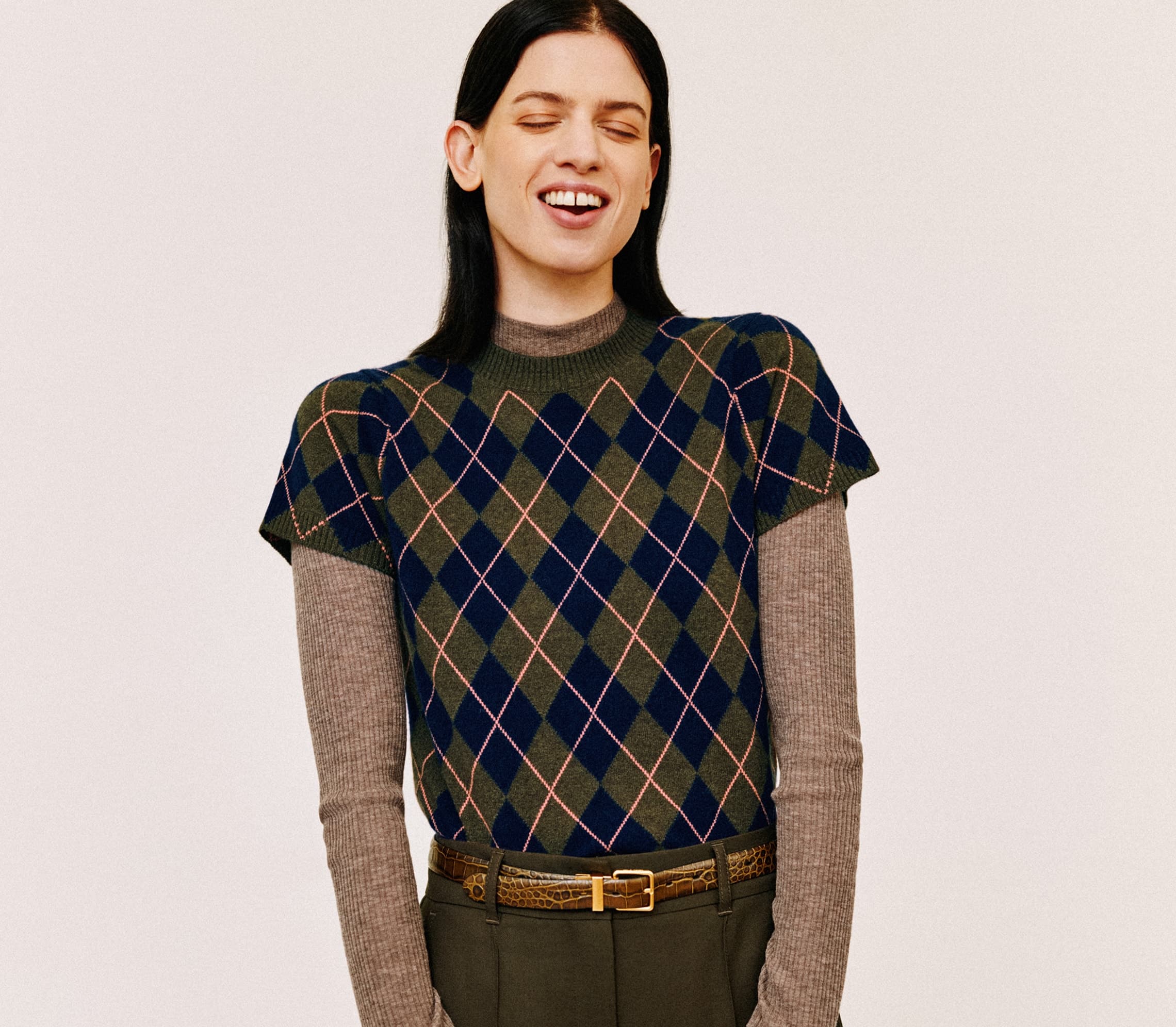 A woman smiling and wearing an argyle patterned jumper in front of a plain background.