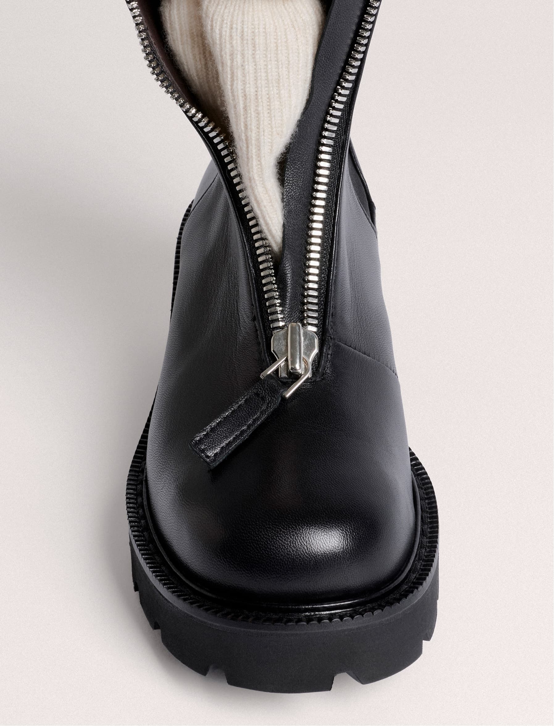 A black leather boot with an unzipped front and a cream sock inside.