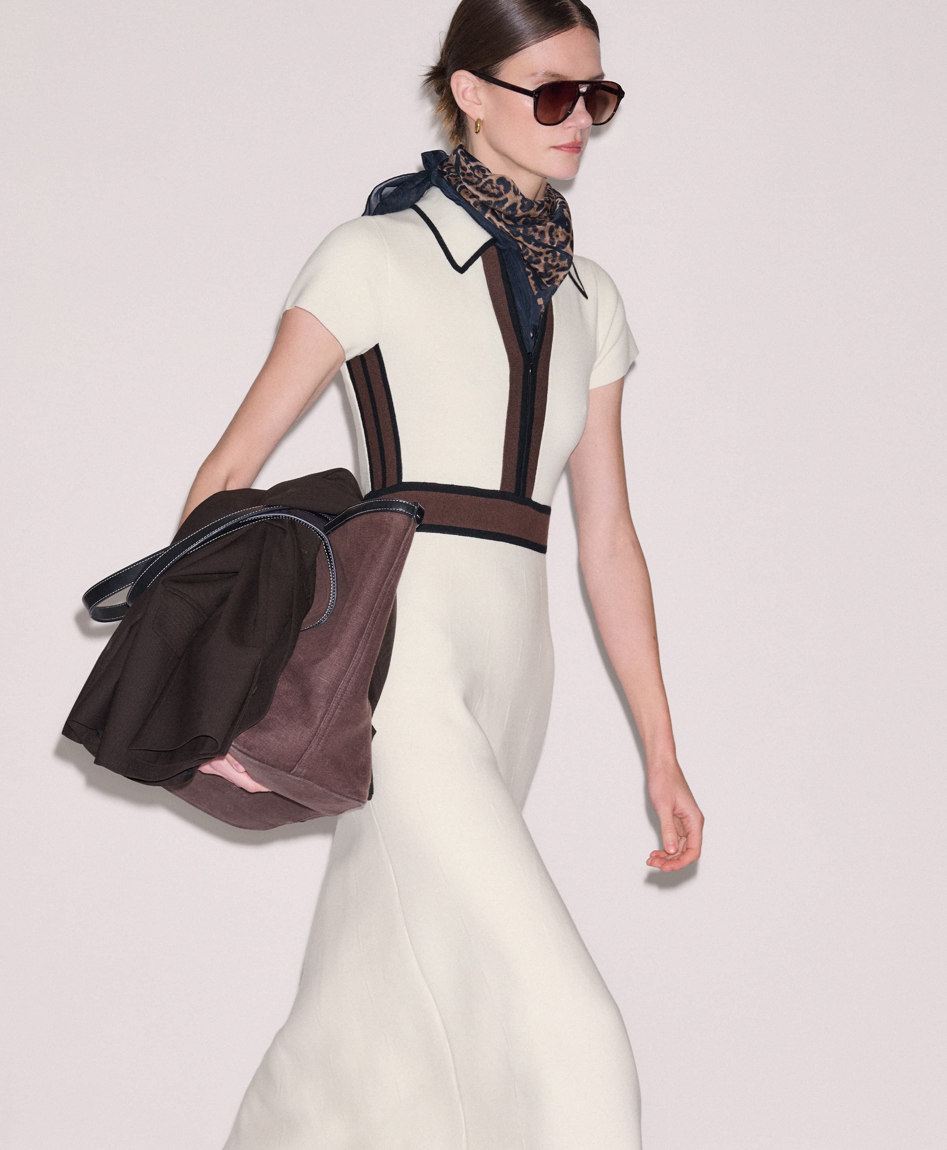 Woman walking wearing a cream dress and carrying a tote bag under her arm.