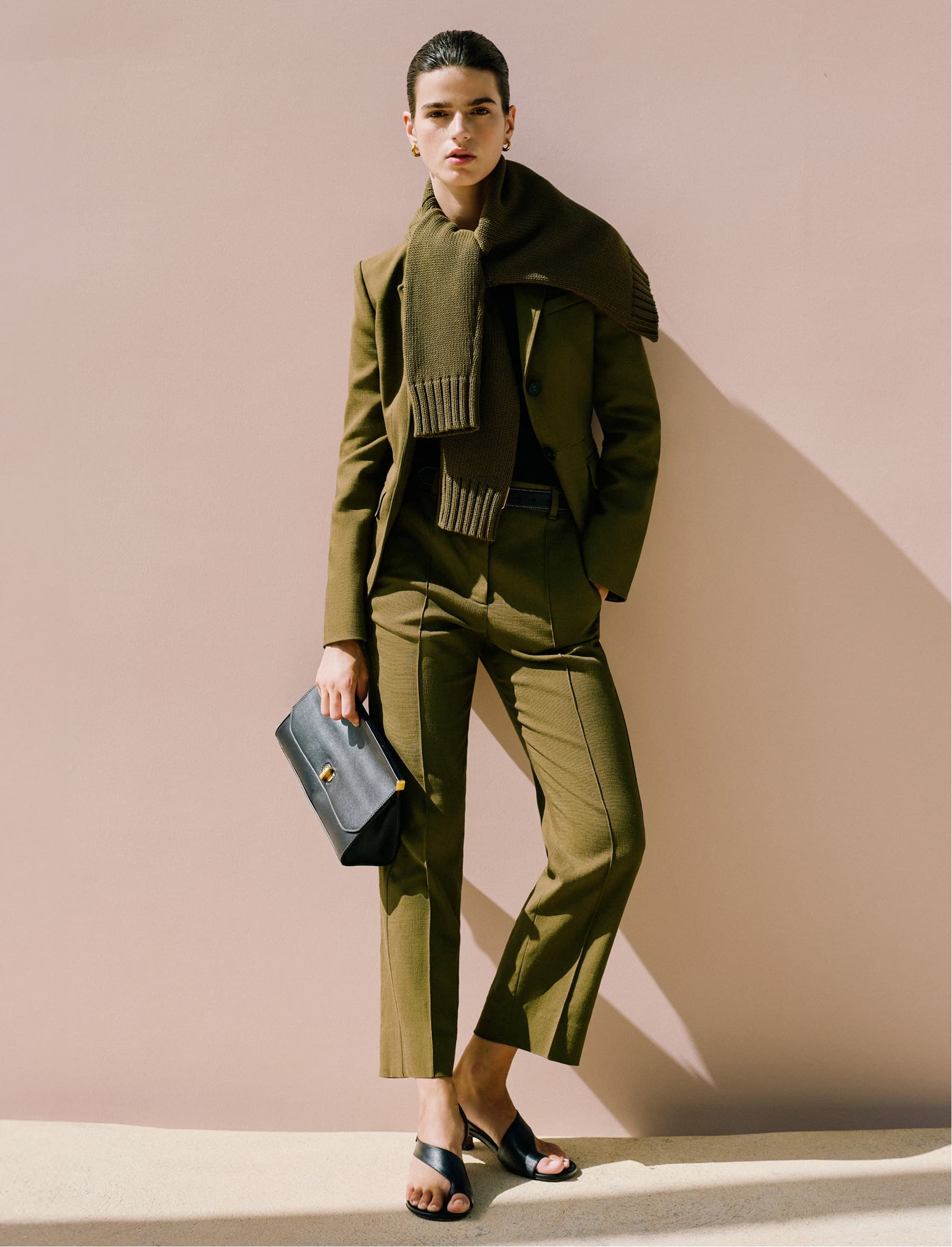 Model posing wearing a green suit, holding a clutch bag.