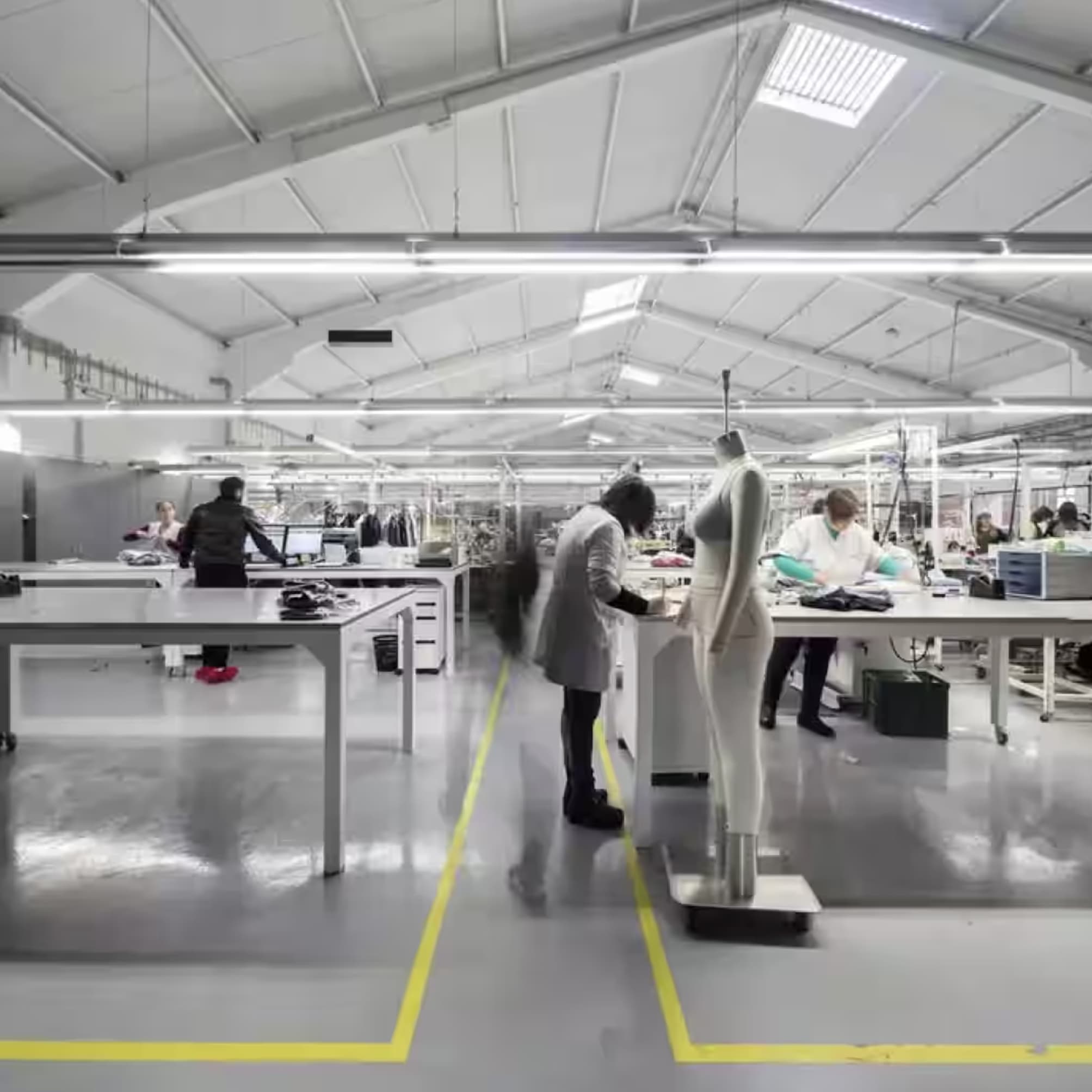 Inside a factory with industrial benches and people working near a mannequin