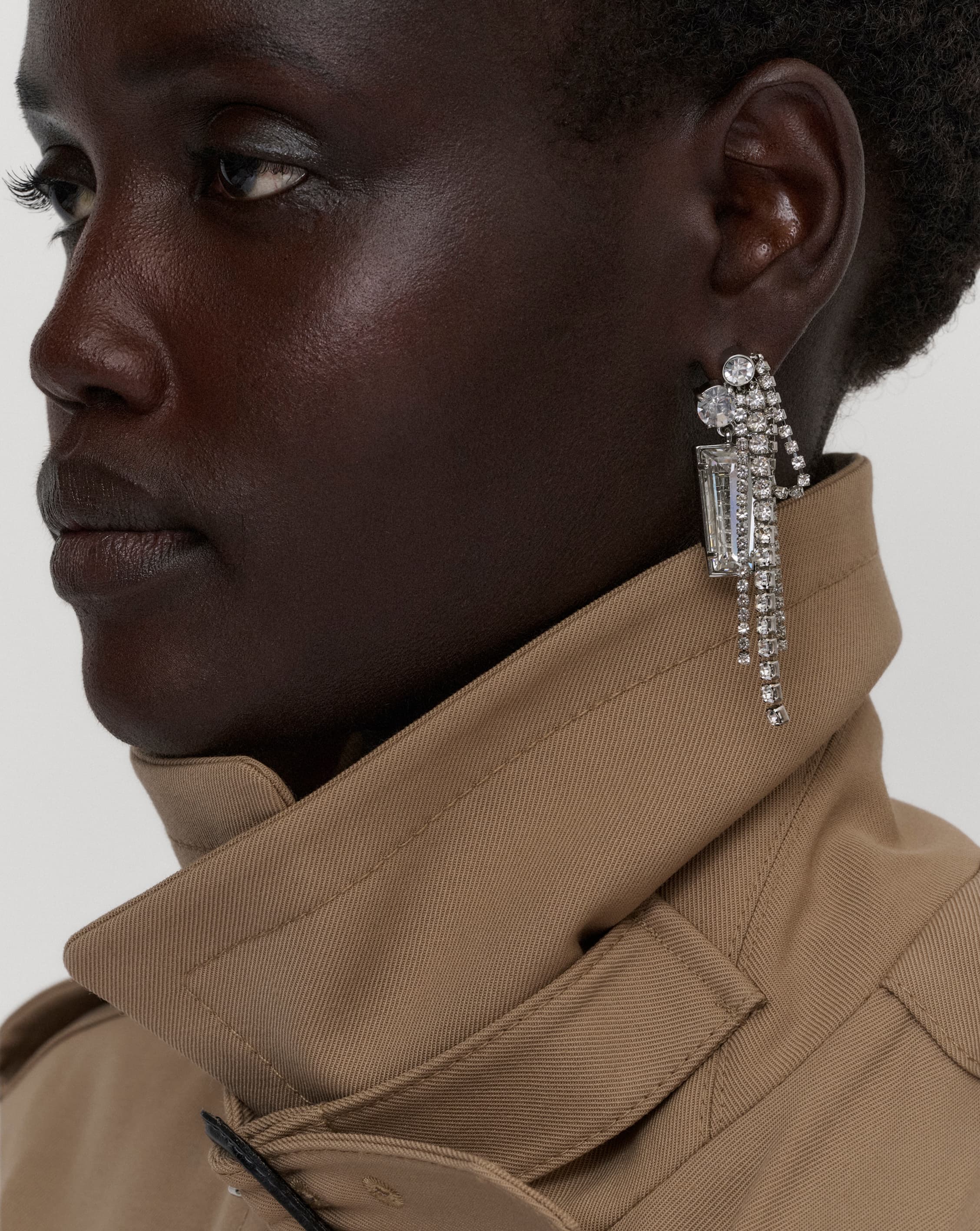 Woman wearing silver cluster earring and trench coat.