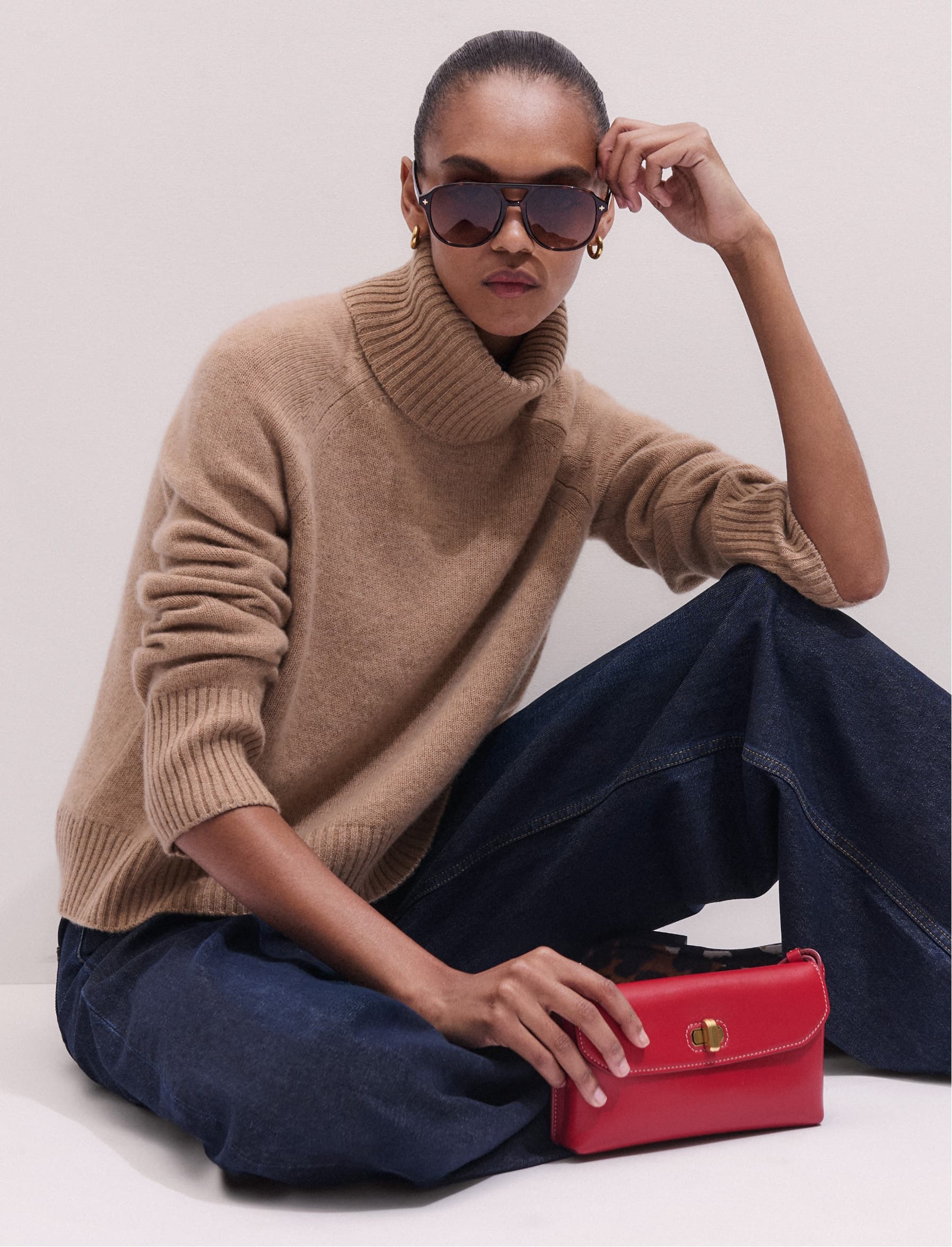 A woman wearing a beige roll neck jumper and sunglasses.