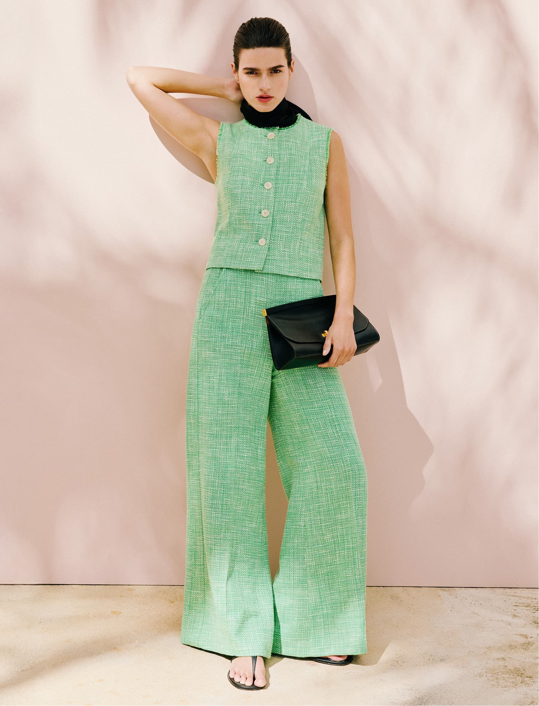 Model posing in a green co-ord, holding a black clutch bag.