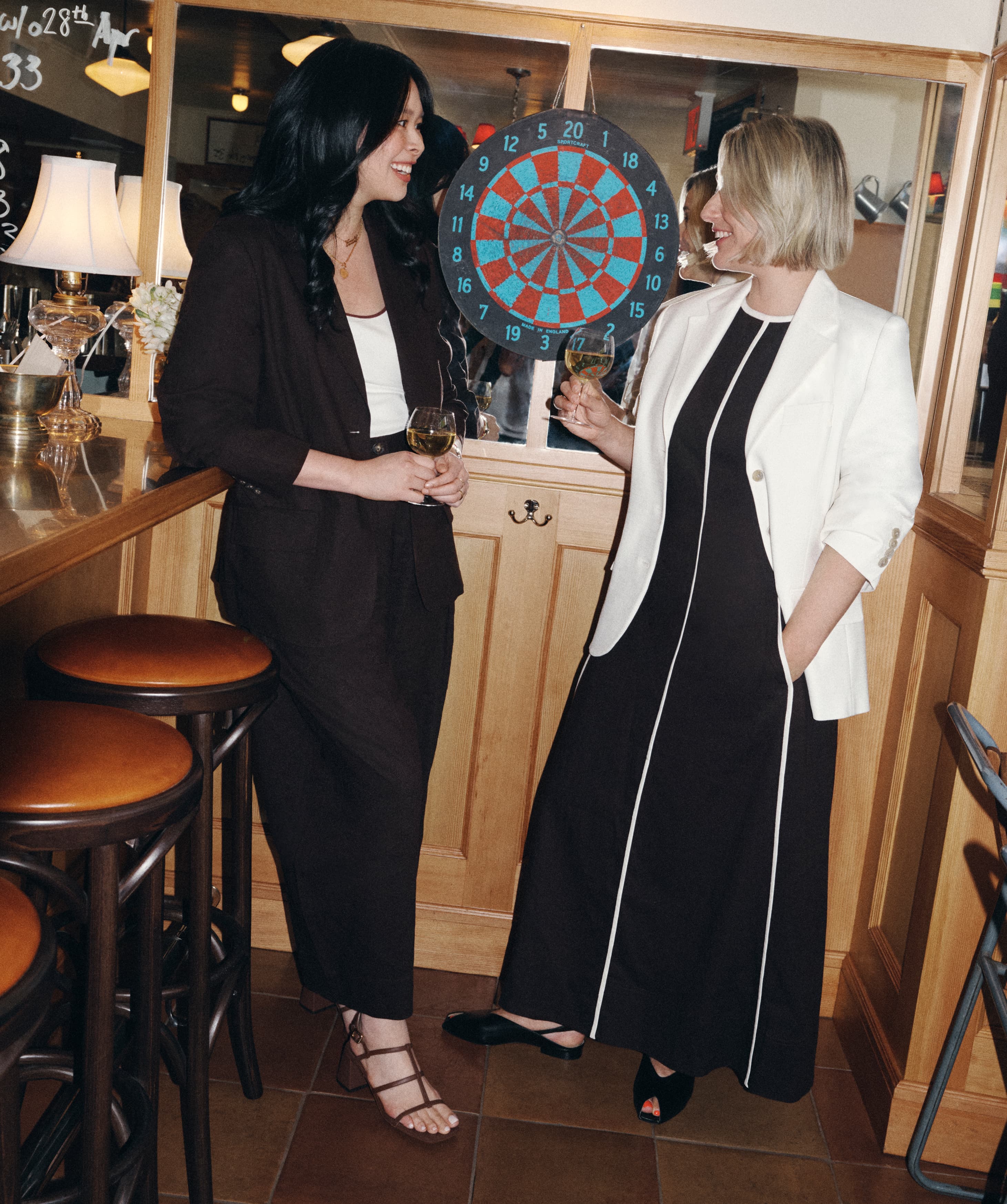 Two women stood in a restaurant, talking and holding glasses of wine.