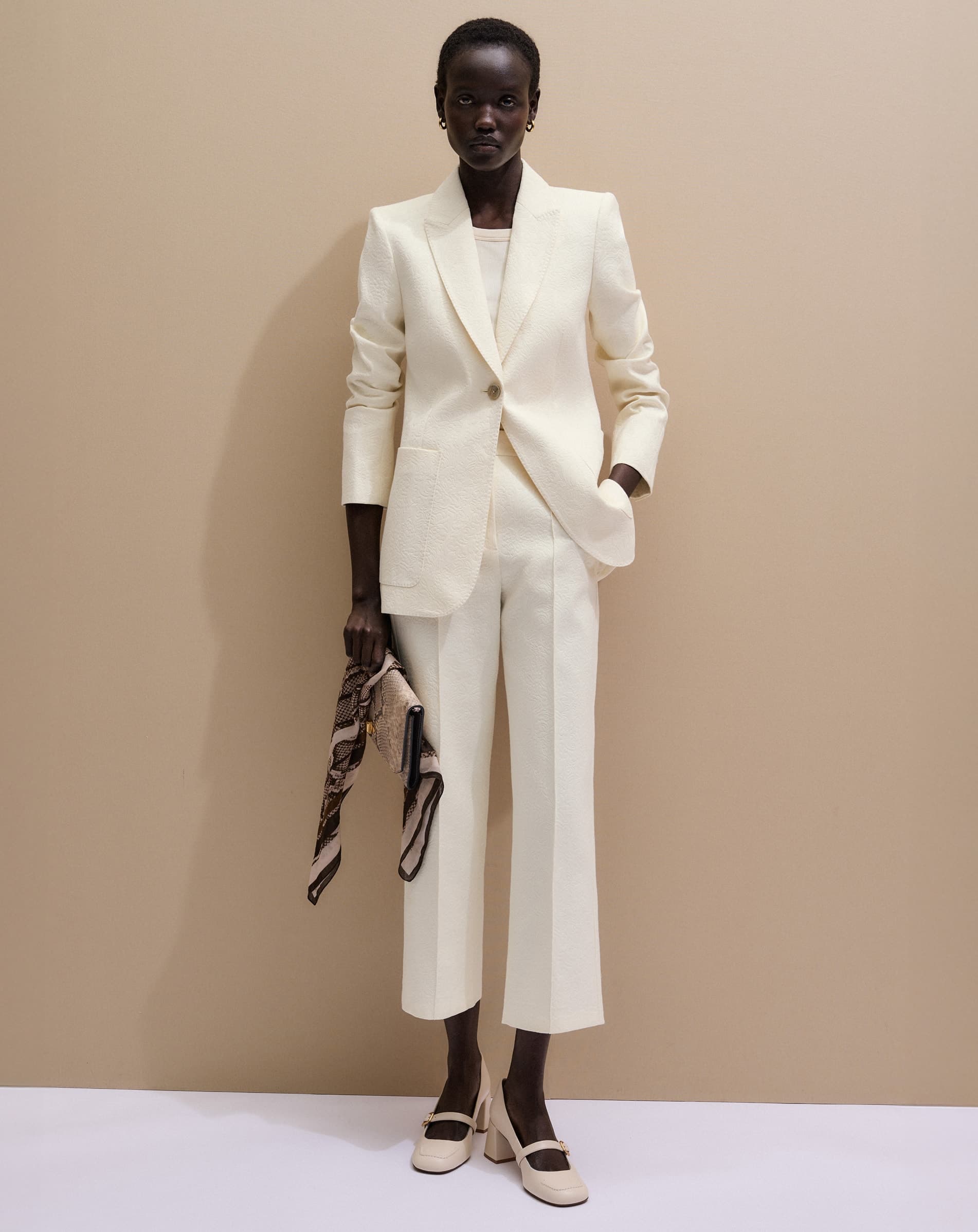 Woman against a beige backdrop wearing a white suit.