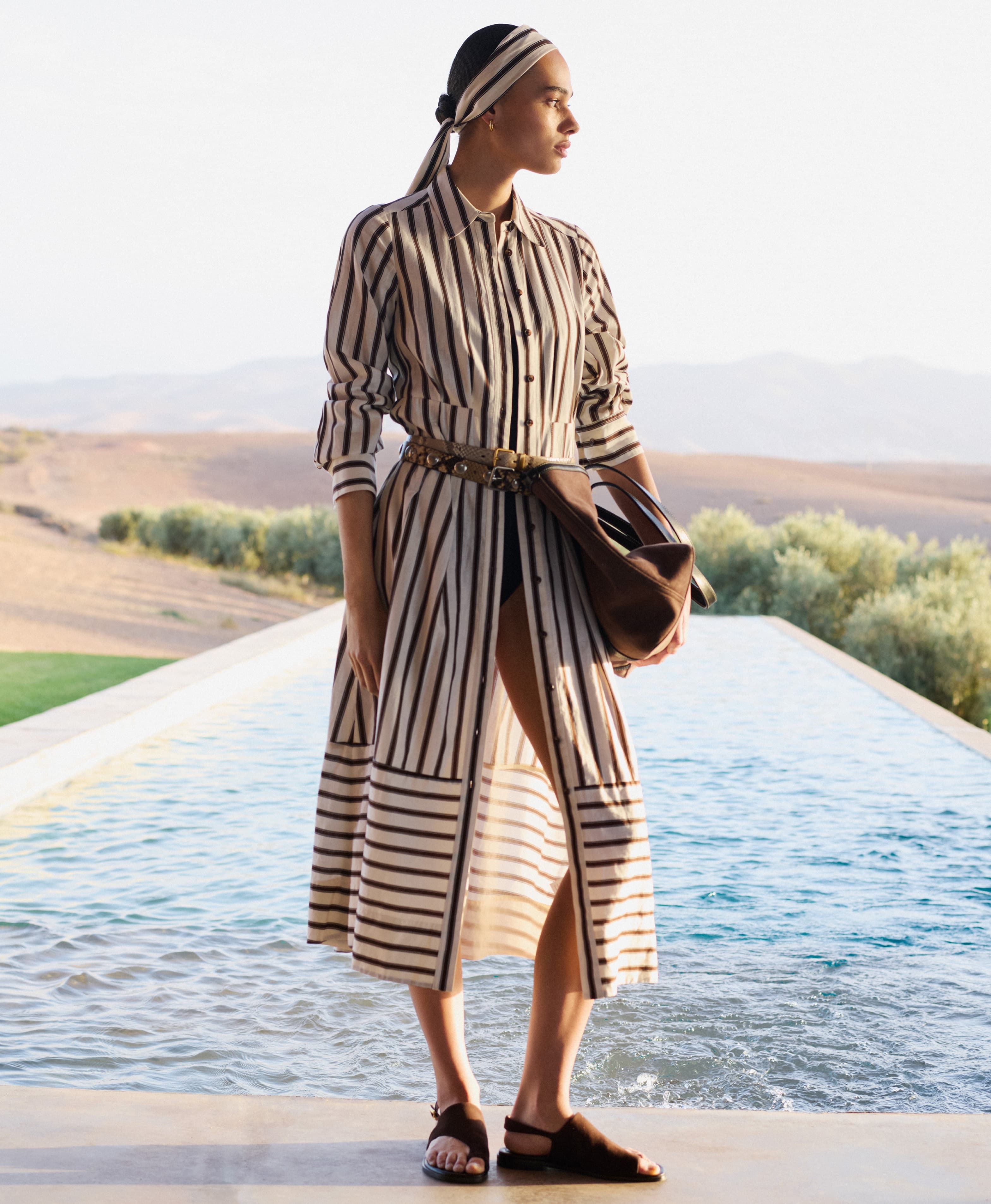Woman wearing a striped dress stood in front of an outdoor pool with a landscape background.