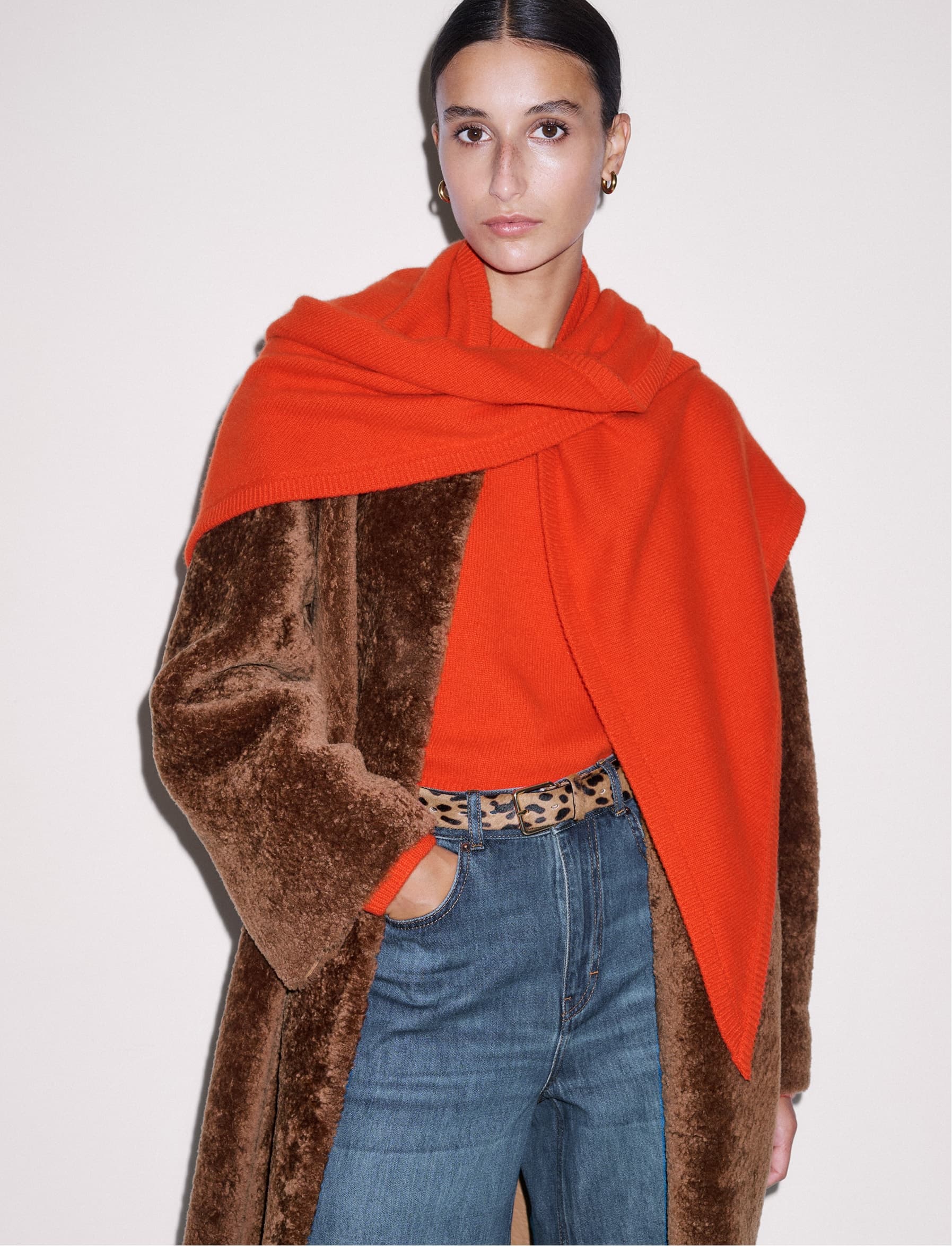 Woman wearing a bright orange scarf and a shearling coat.