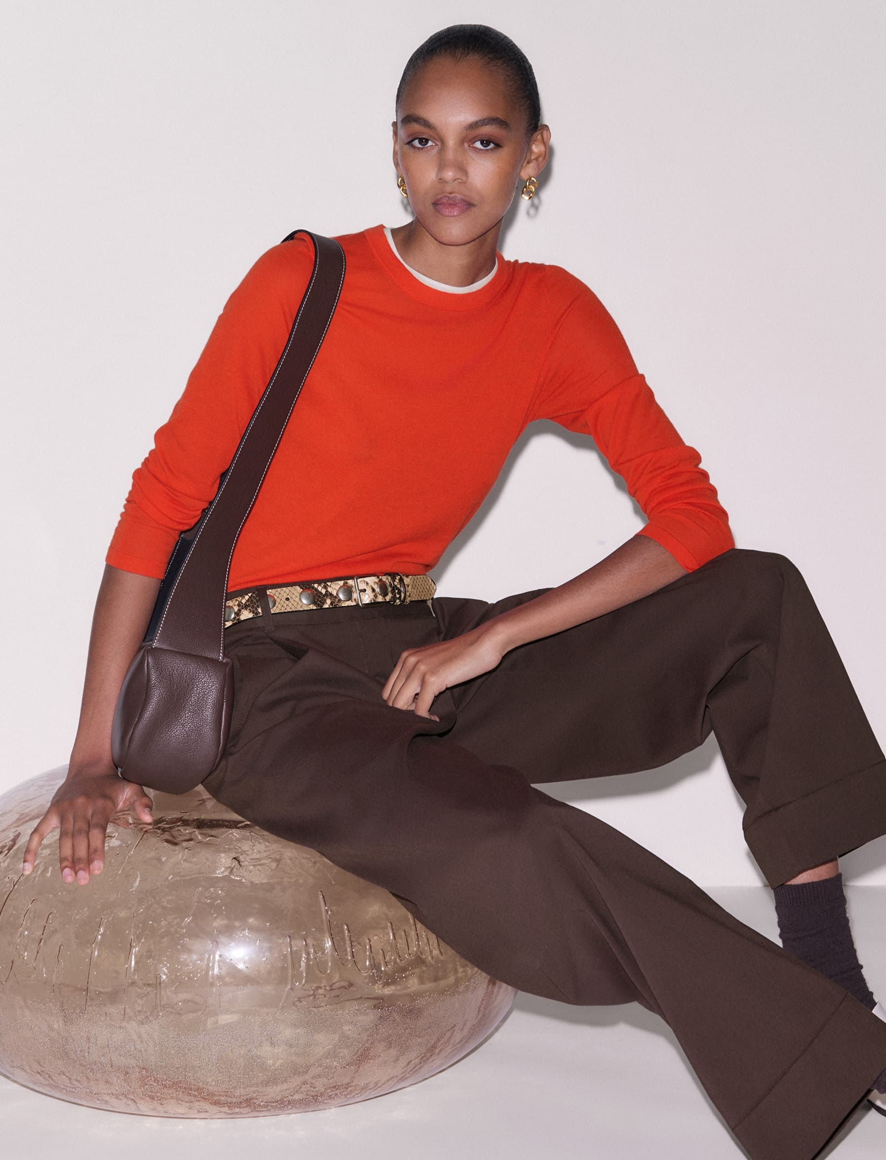 Woman sat on a stool wearing a bright orange jumper.