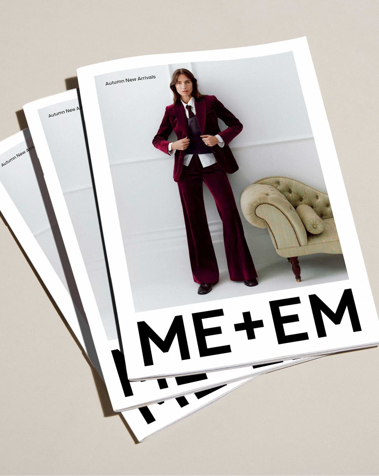 ME+EM lookbook with model standing wearing red velvet suit with tie and white shirt, standing next to a cream sofa