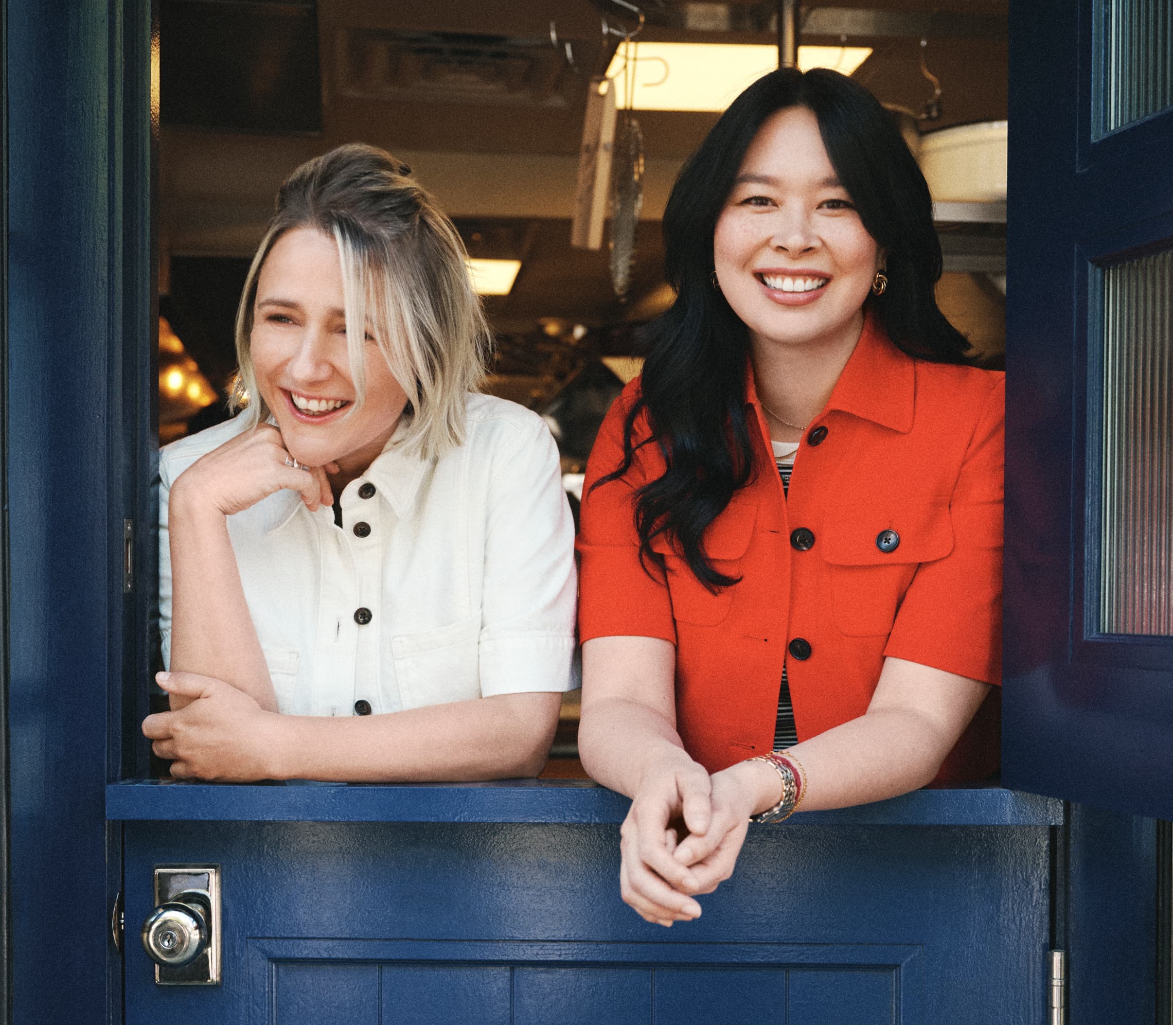 Two women stood in a window frame, one wearing a white jacket, the other wearing a red jacket.