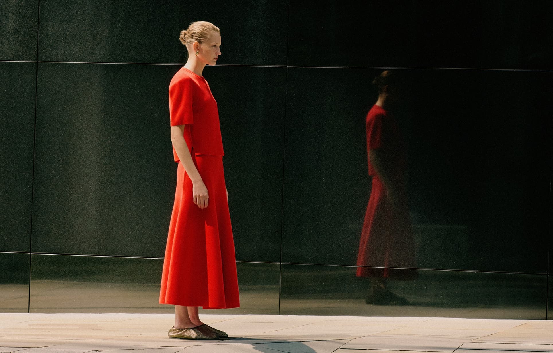 Model standing side on wearing red matching top and skirt with gold mesh shoes