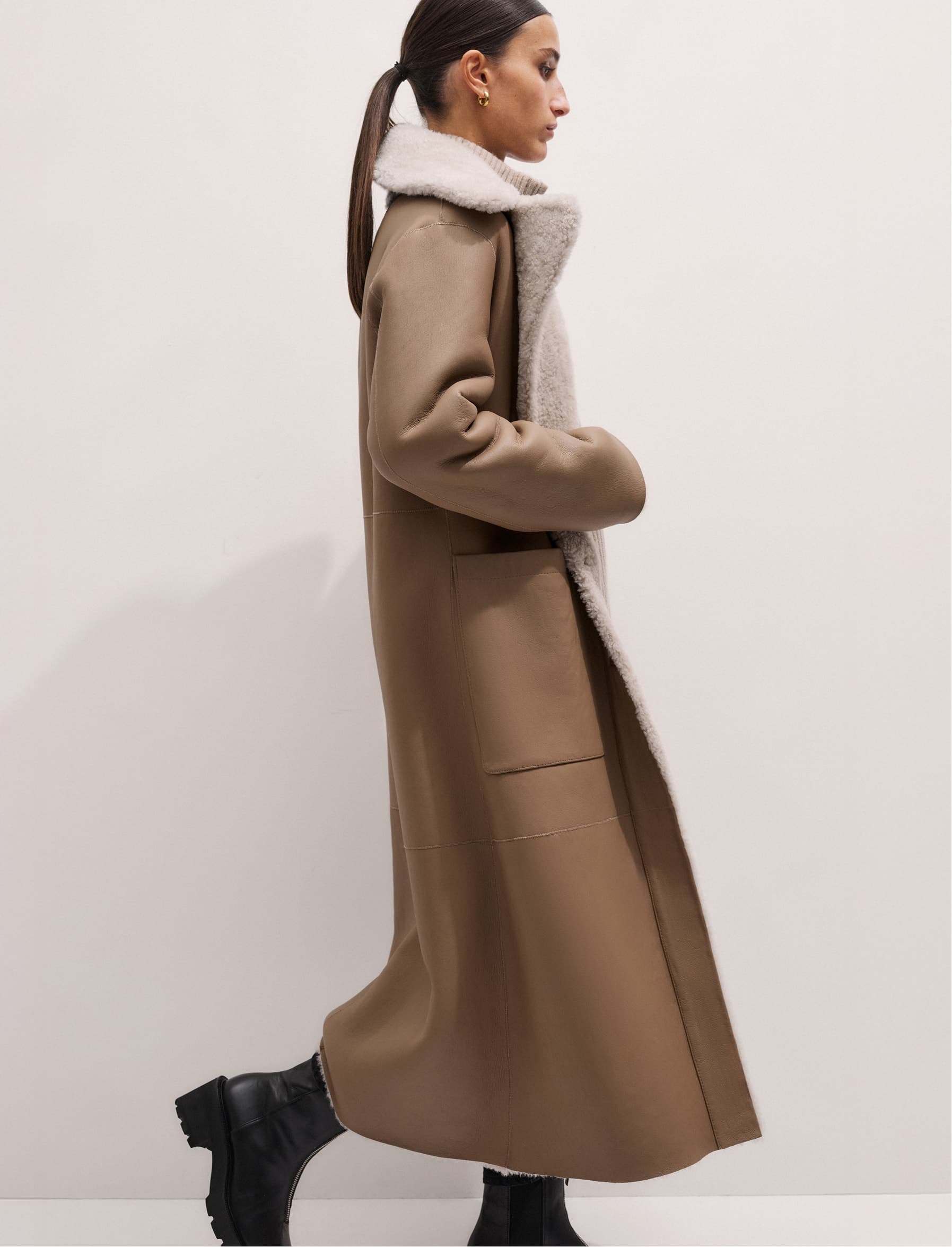 A woman walking and wearing a long shearling jacket facing side-on to the camera.