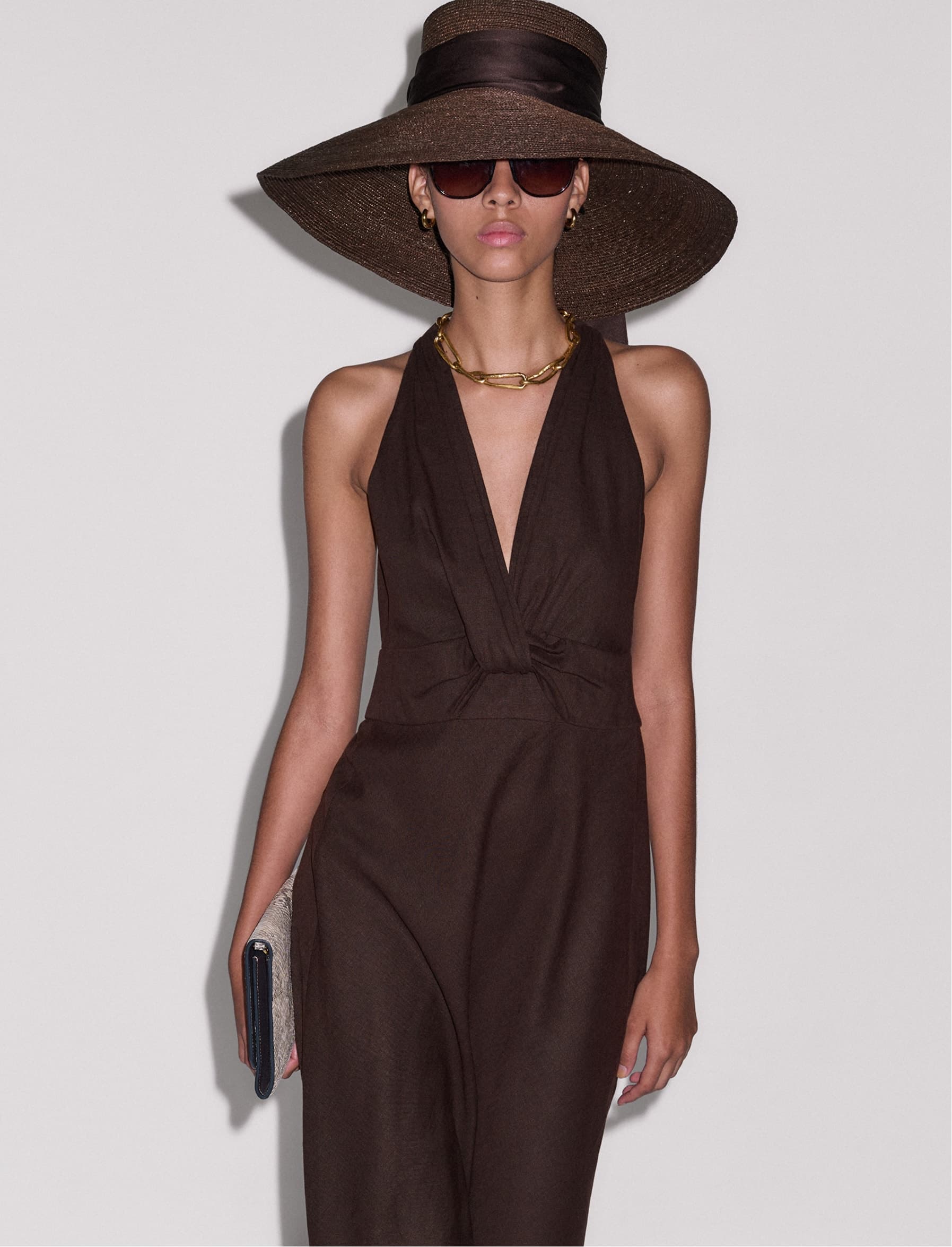 Model wearing a brown hat and brown dress, holding a clutch bag..